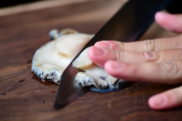 Hand with knife cutting abalone meat